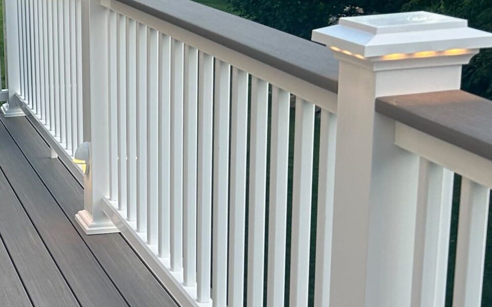 Lit post-cap and post-side lights on a white deck railing at dusk