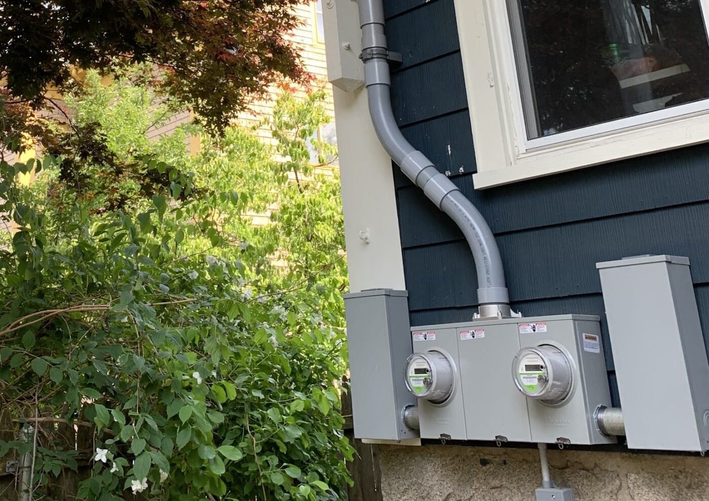 Service conduit running down to a new two-meter bank on a blue clapboard wall