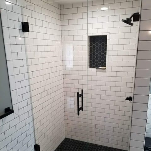 Subway-tiled walk-in shower with a frameless glass door and a recessed ceiling light