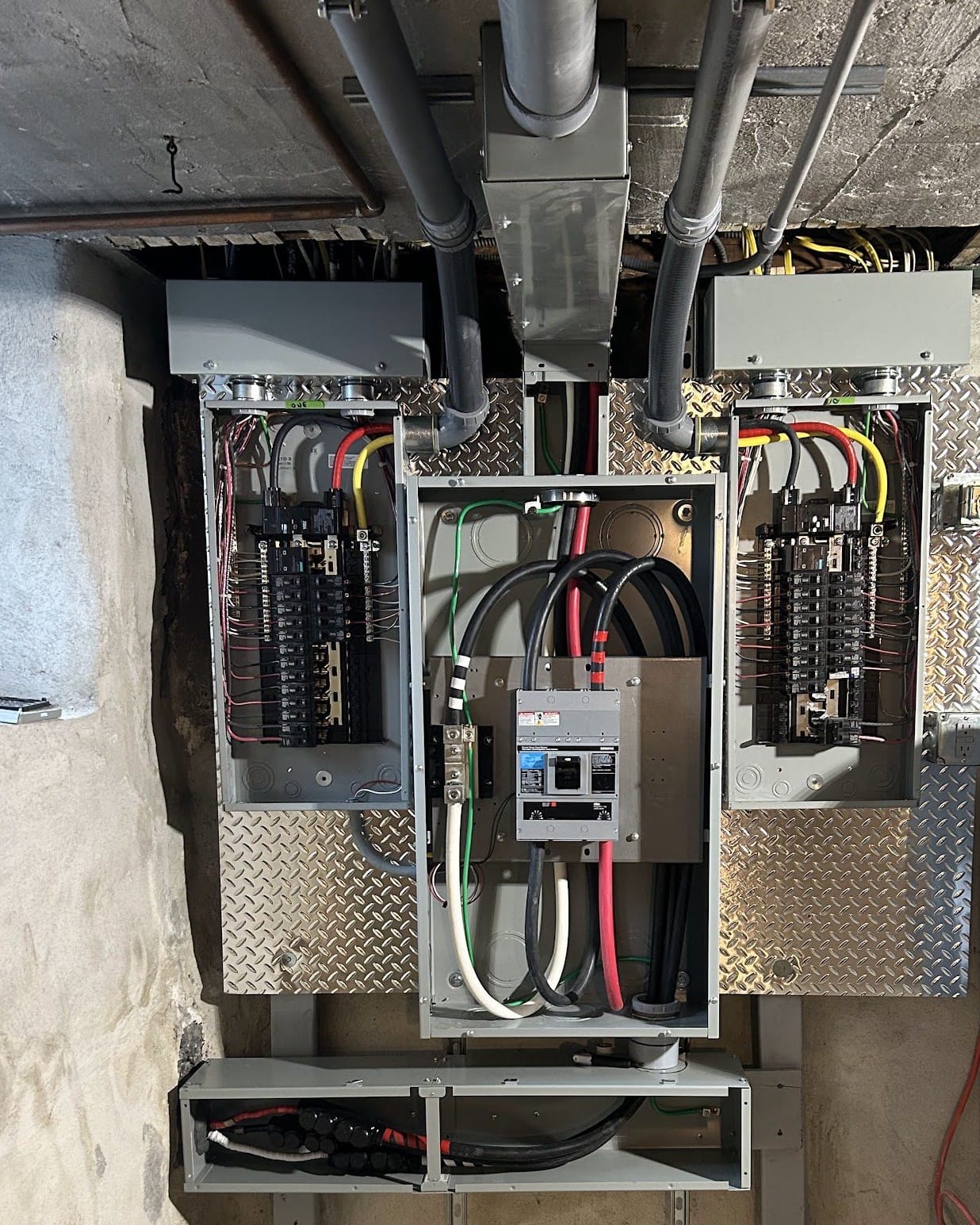 New main breaker enclosure between two breaker panels on a diamond-plate backboard, installed by Colonial Electric