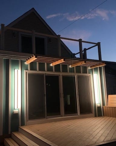 Vertical exterior wall lights glowing beside sliding doors on a rear addition at dusk, a Colonial Electric job